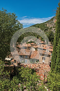 View of trees and house roofs under sunny blue sky in Moustiers-Sainte-Marie.