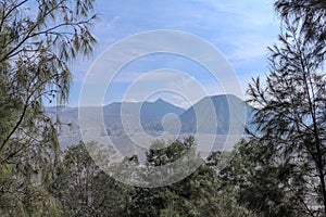 View through the trees and mountain vegetation of the crater of the active volcano Bromo and the photogenic Mount Batok in close