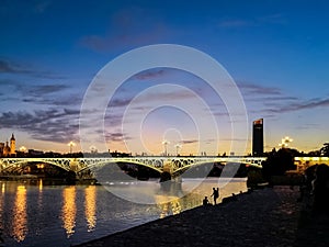 View of the Triana Bridge Bridge of Isabel II spanning the Guadalquivir River in Seville illuminated at dusk.