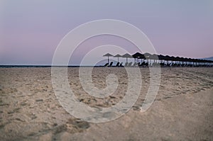 View of tropical beach with big straw umbrellas on the sunset sea background