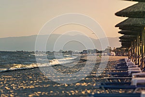 View of tropical beach with big straw umbrellas and sun loungers on the sunset sea background