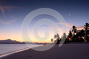 View of tropical beach, coconut trees and resort during sunrise