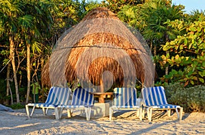 View of a tropical sandy beach with straw umbrellas and lounge chairs.