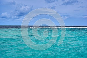 View of turquoise sea at Coco Bodu Hithi resort in Maldives with distant waves and blue sky with magnificent clouds.