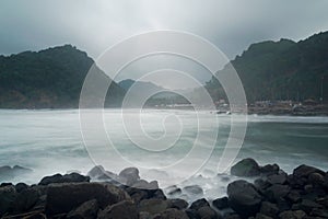 The view of two hills lined with dense and green trees located on the beach which has clear and refreshing water. Photos were take