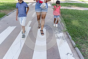 Two kids walking with their mother outdoors in a pathway in a park.