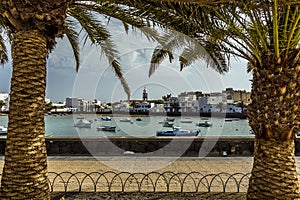 A view between two palm trees of small boats moored in the lagoon of Charco de San Gines in Arrecife, Lanzarote