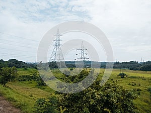 View of two powerline towers standing on a green meadow on a gloomy day background