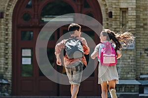 View of two schoolkids with backpacks running in schoolyard