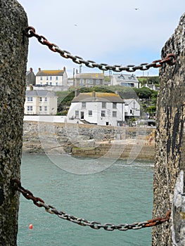 View through two stone posts connected by a chain to houses at the harbor of Porthleven Cornwall England