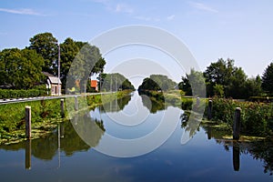 View on typical dutch endless straight waterway canal lined with green grass and trees in countryside