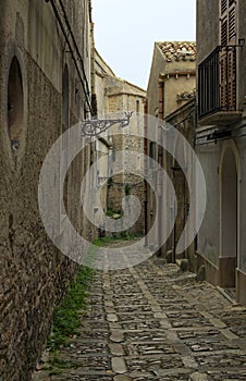 View of typical narrow pedestrian medieval cobblestone street along ancient buildings in historical part of Erice village, Sicily