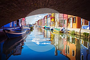 View under bridge of colorful Venetian houses and boats at Islands of Burano in Venice, Italy