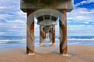View under an ocean pier with cloudy blue sky