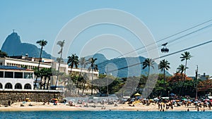View of unidentifiable people at Praia Vermelha Beach in Rio de Janeiro, Brazil with Corcovado mountain and sugarloaf cable car in