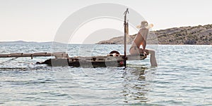 View of unrecognizable woman wearing big summer sun hat tanning topless and relaxing on old wooden pier in remote calm