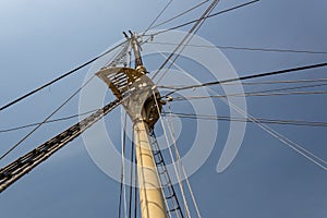 View up the main mast of a large sailing vessel, rigging and shrouds fanning out against a dark sky