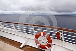 View from upper deck of modern cruise ship showing lifesaver ring and teak railings on a grey stormy day in the Tropics