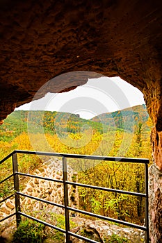 a view of a valley from a cave entrance in a mountain area with a fence and a railing in the foreground