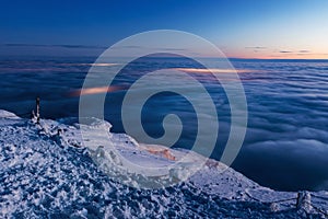 View of the valley from the summit of Snezka. Inverted clouds in the valley, shining cities under the clouds. The peak of the Snez