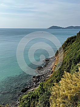 View of a vast turquoise ocean from a rocky cliff overlooking a grassy shoreline in Samet Island