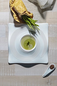 View of a vegetable soup dish with asparagus surrounded by a paper bag full of fresh asparagus