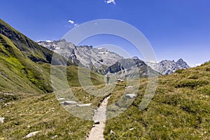 View of a very large and majestic alpine landscape in the Lord of the Rings style. In the foreground a girl walks toward