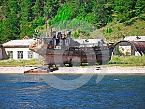 View of the village of Listvyanka from the lake Baikal. an abandoned rusty dilapidated useless ship on the beach