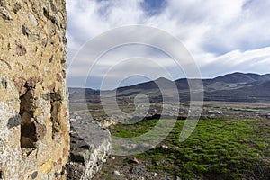 View of the village and mountains from the Medieval fortress on a rock. Stone wall and part of tower. Bright blue sky with clouds