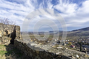 View of the village and mountains from the Medieval fortress on a rock. Stone wall and part of tower. Bright blue sky with clouds