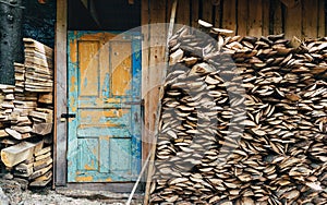 View at a village storage house for tools and fire woods. Vintage painted door in blue color. Paint is partially pilled off.