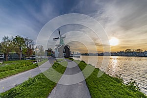 View of a village street that ends at a working mill on the river Zaan at sunset . photo