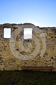 View of wall of ancient fortress with arched loophole windows against blue sky. There is rest bench near old stone wall. Tourism photo