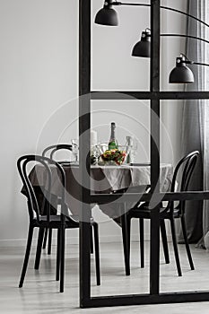 View through the wall with muntins on elegant dining room table covered with grey tablecloth