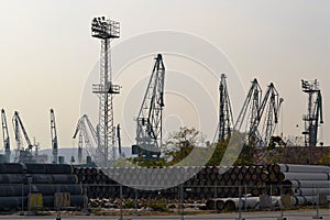 View of the warehouse of pipes and harbor cranes in the seaport on an autumn evening