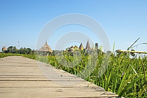 View of Wat Tham Sua with bamboo bridge, long walkway in the middle of lush rice fields, blue sky and sunshine in Thailand.