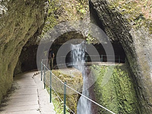 View of waterfall crossing the path at levada, water irrigation channel and tropical plants at hiking trail Levada do