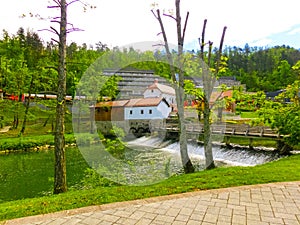 View on waterfall, mill in white building, pedestrian bridge in Park Postojna jama near Postojna Cave