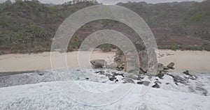 View of the waves crashing against a flying reef over a white sand beach under a hill, raw footage, ungraded, no color, log