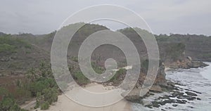 View of the waves crashing against a flying reef over a white sand beach under a hill, raw footage, ungraded, no color, log
