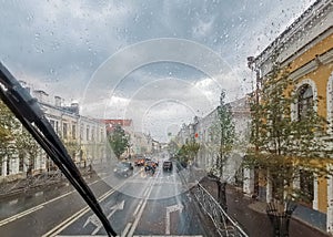 View of the wet city street and the road through the windshield in the rain drops