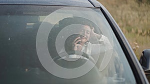 View through wet with rain windscreen of smiling girl in car talking on phone
