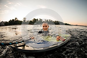 view of wet woman in wetsuit in the water leaning on wakeboard