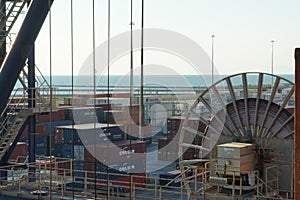 View on wheel with cable of gantry crane in container terminal with stowed containers from different shippers in Livorno.