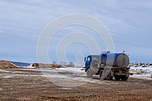 View from a wheel of the off-road truck riding in a dirt road on cloudy sky background. Scene. Close up for red cab of a lorry