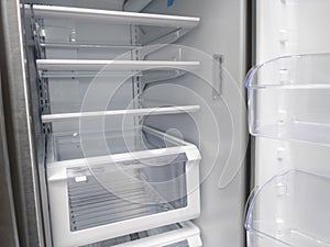 View of a white, empty fridge with the door wide open to see several shelves and drawers