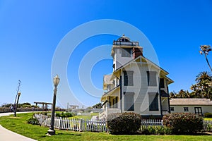 A view of a white and green lighthouse in the park with a white picket fence surrounded by lush green grass and trees