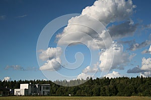 View on white house and forest and sky with clouds