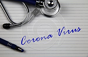 View on white index card with stethoscope and blue ball pen with words corona virus