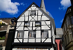 View on white medieval timbered house facade with catholic church clock tower in summer with blue sky